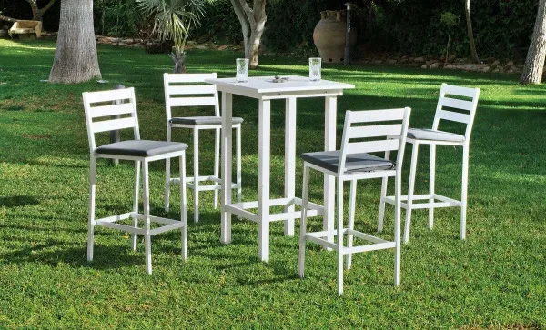 Mesa alta cuadrada fabricada en aluminio. Pintada en color blanco. Está en una terraza al exterior.